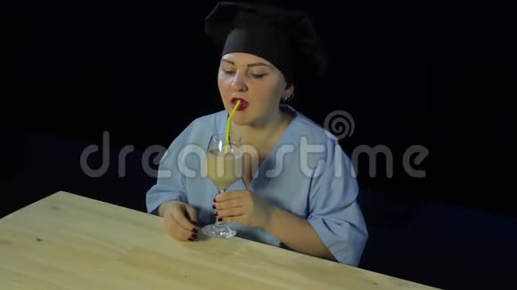 一位黑色背景下的女厨师品尝水果奶昔并展示班的签名视频的预览图