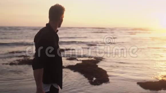 年轻人穿着时尚的现代服装背包在海洋海滩观看金色日落慢动作视频的预览图