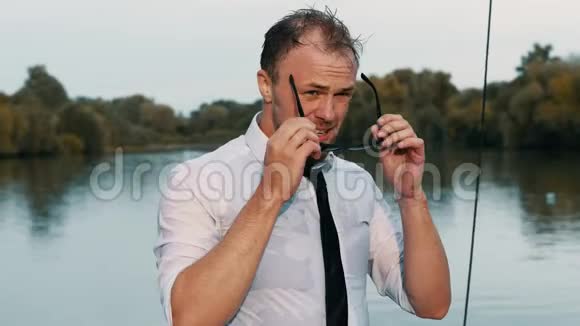 一位身穿西装领带戴着时髦太阳镜日落度假的英俊湿漉漉商人的特写肖像视频的预览图
