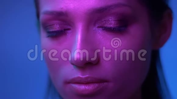 未来时尚模特在紫色的霓虹灯闪烁着闪光的妆容静静地观看着镜头视频的预览图