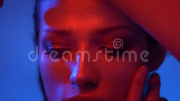 时尚模特穿着红色和蓝色霓虹灯的特写镜头用手指和手表遮住她的脸视频的预览图