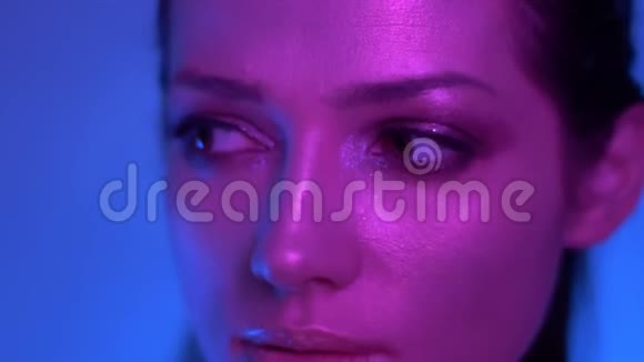 未来时尚模特在彩色紫色和蓝色霓虹灯摆成相机在演播室观看向左视频的预览图