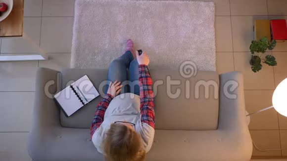 年轻怀孕女性坐在沙发上拿着遥控器看电视的特写镜头视频的预览图