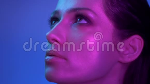 时尚模特在紫罗兰色的霓虹灯慢慢移动和关闭眼睛以显示闪光的化妆在工作室视频的预览图