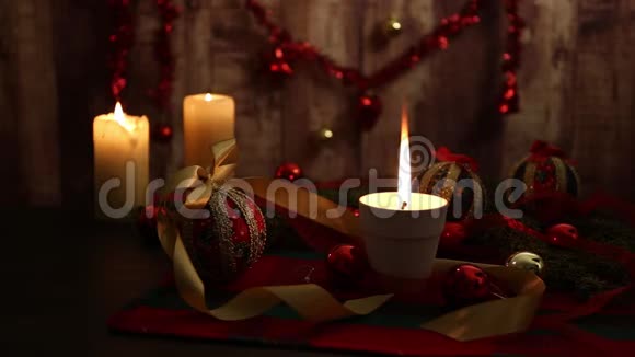圣诞节的气氛三支点燃的蜡烛一支在前景上有大火焰的蜡烛红色和金色的脱钩的球缎子金色的丝带视频的预览图