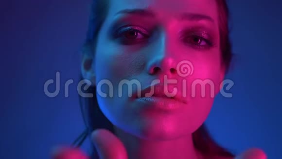 蓝色和粉红色霓虹灯美丽模特的特写镜头仔细地看着镜头伸出它的手视频的预览图