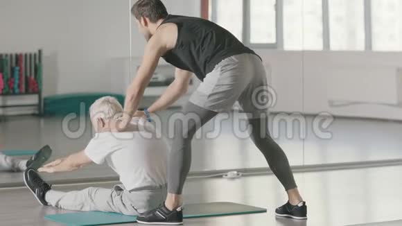 体育教练帮助退休男子在健身俱乐部做伸展运动视频的预览图
