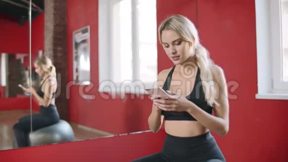 美丽的女人在健身俱乐部使用智能手机微笑健康的女人休息视频的预览图