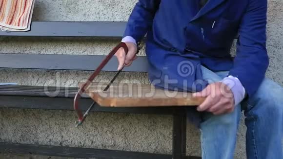 老人的手在野餐时用木头手锯在外面的地面上切割木板视频的预览图