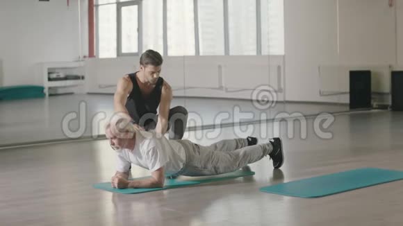 健身教练帮助老年人训练体育俱乐部的木板练习视频的预览图