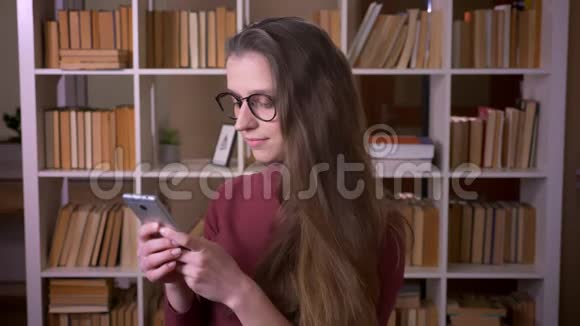 戴着眼镜的年轻白种人女学生的特写镜头她用手机笑着开心地看着镜头视频的预览图