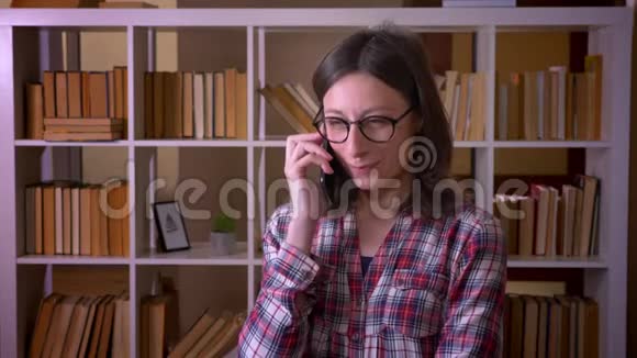 在室内图书馆打电话的戴眼镜的年轻漂亮女学生的特写镜头视频的预览图