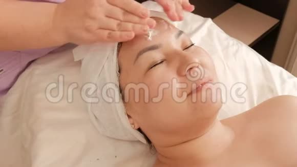 美容师将白色奶油涂在美容院中年亚洲妇女的脸上振兴放松和愈合视频的预览图