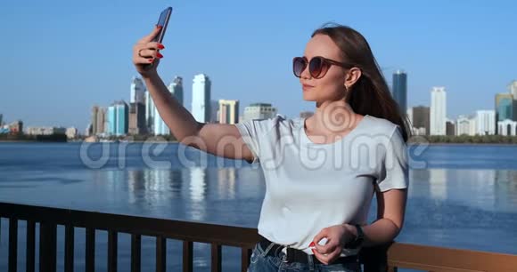 夏天大城市和海滨背景的女孩在智能手机上自拍视频的预览图