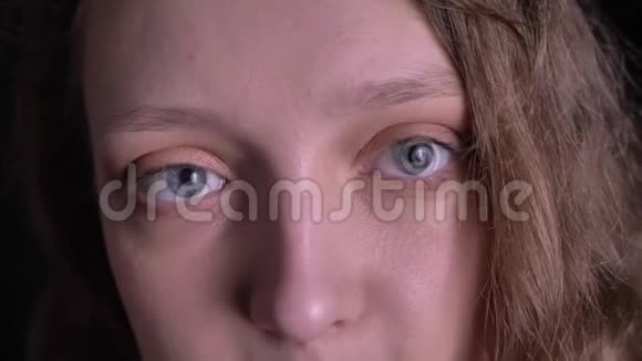 一个年轻的卷发女孩的特写眼画像专注地看着镜头在黑色背景下向它眨眼视频的预览图