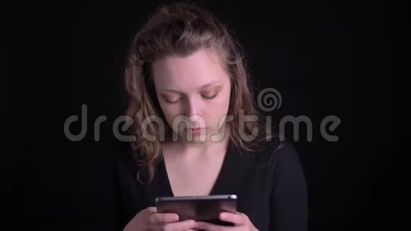 一幅年轻卷发女孩专注地看着平板电脑并在黑色屏幕上显示绿色屏幕的画像视频的预览图