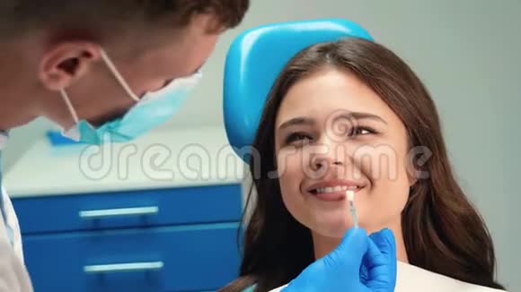 戴口罩和手套的年轻牙医使用搪瓷刻度为微笑的黑发病人妇女在手术期间取合适的阴影视频的预览图