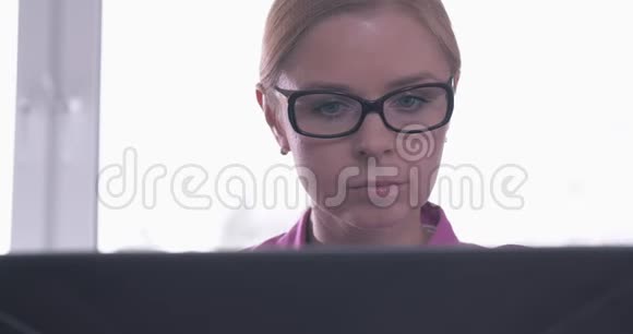戴眼镜的微笑女人在笔记本电脑上工作的肖像视频的预览图