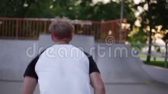 一个穿着宽大的黑色裤子头发上有一条红色绷带的金发小伙子在溜冰鞋上跑着漂亮的筋斗视频的预览图