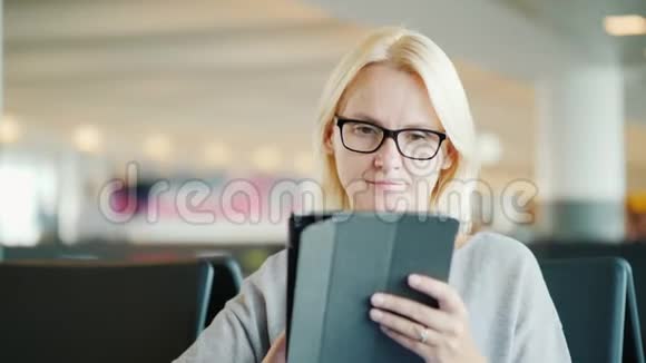 戴眼镜的女人的肖像在汽车站的候车室用平板电脑视频的预览图