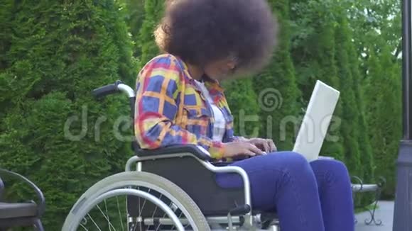 肖像微笑的非裔美国妇女发型是非洲裔残疾的轮椅使用笔记本电脑看视频的预览图