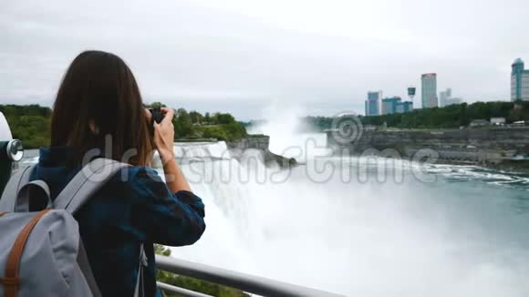 带着相机拍摄史诗尼亚加拉大瀑布的兴奋记者女子的后景环顾四周微笑的慢动作视频的预览图