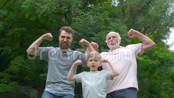幸福家庭的肖像爷爷父亲和儿子微笑着在公园的背景下展示他们的肌肉视频的预览图