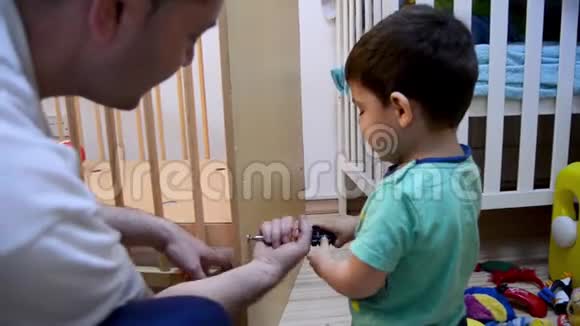 可爱的两岁男孩帮助他的父亲为他的小弟弟放下小床视频的预览图