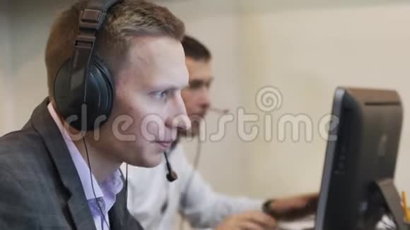 男性呼叫中心代理在无线耳机咨询在线客户端利用电脑商人们在谈话视频的预览图