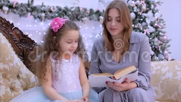 圣诞夜年轻快乐的母亲和女儿坐在壁炉旁在圣诞灯和视频的预览图