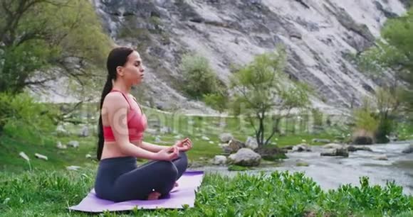 美丽的年轻女子在大自然中间的垫子上练习瑜伽她有一个冥想姿势视频的预览图