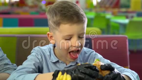 小孩戴着黑手套吃汉堡看着摄像机视频的预览图