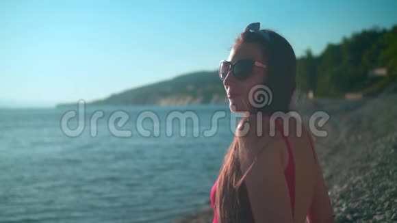 一个漂亮的年轻女孩穿着红色的一件泳衣和眼镜坐在海滨视频的预览图