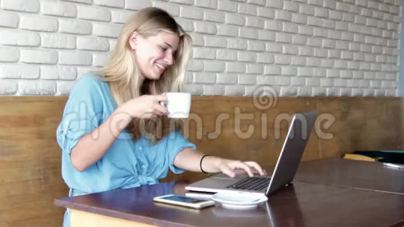 年轻漂亮的金发女人坐在咖啡馆里用她的笔记本电脑视频的预览图