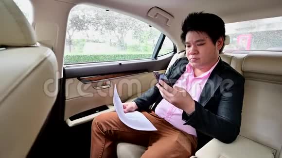 4位亚洲商人坐在车里一边用手机聊天一边看文件视频的预览图