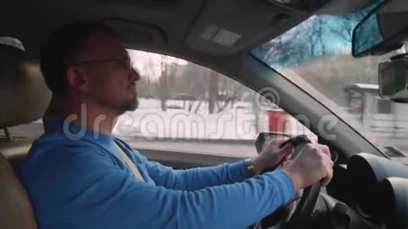 穿着蓝色衬衫的白色司机驾驶着覆盖着雪和遮阳板的城市汽车视频的预览图
