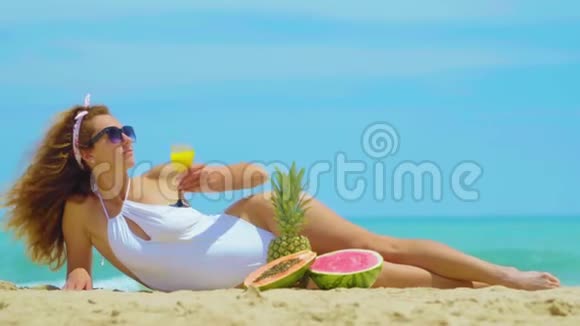 女人喝新鲜橙汁背景海年轻的美女躺在海边的沙滩上喝酒视频的预览图