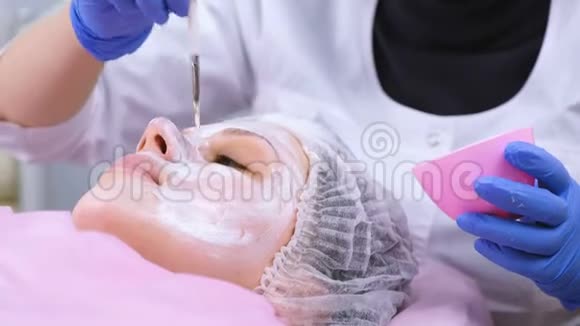 美容师用刷子把面具戴在女人脸上滋润的脸面的特写视频的预览图