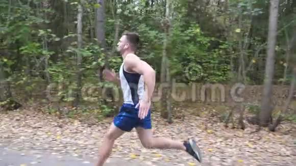 英俊强壮的运动员带着无线耳机沿着森林附近的小径快速冲刺在路上奔跑的运动员视频的预览图