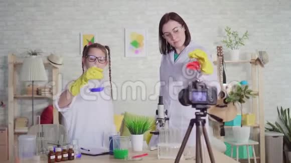 一位年轻女性和一位十几岁的女孩博客作者在化学实验室学校的项目混合试剂给五个调查一下视频的预览图