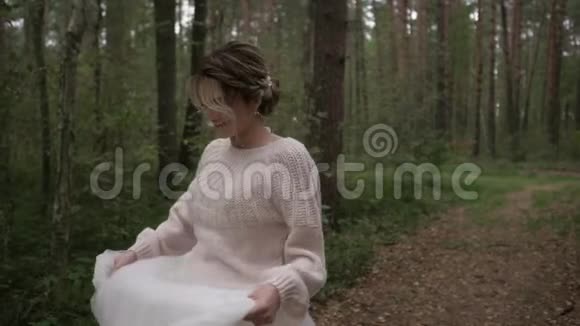 一位美丽的年轻开朗快乐的新娘穿着婚纱和一件精致的毛衣在森林里奔跑和旋转慢慢视频的预览图