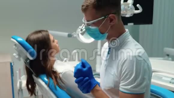戴着医疗手套和戴着眼镜的年轻牙医准备检查年轻的黑发女子病人视频的预览图