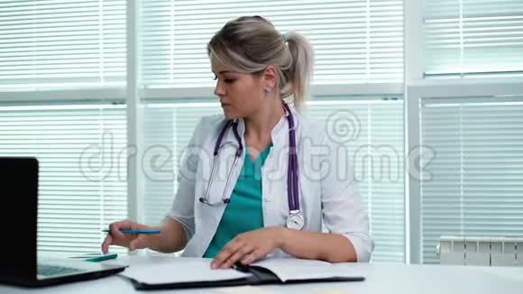 年轻的女医生坐在桌边记录与工作有关的数据视频的预览图