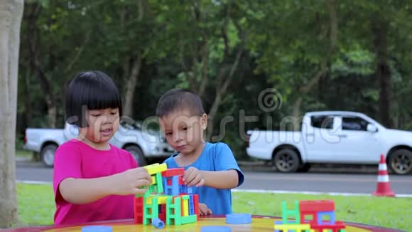 男孩和女孩建造了一座玩具塔里面有五颜六色令人兴奋的积木并在萨拉纳花园的桌子旁拍打着它视频的预览图