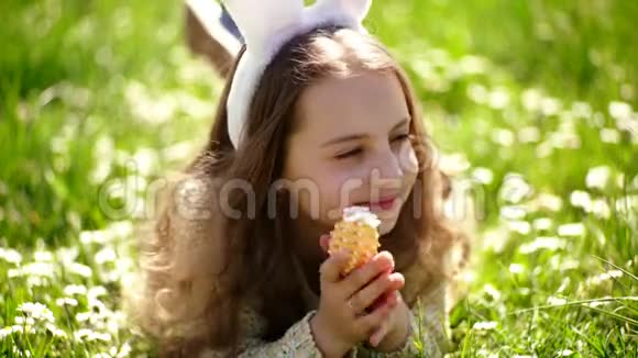 可爱的小兔子耳朵躺在草地上复活节春天花园里寻找复活节彩蛋的小女孩视频的预览图