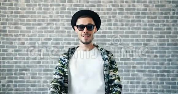 戴帽子戴太阳镜的人在砖墙背景上跳舞的肖像视频的预览图