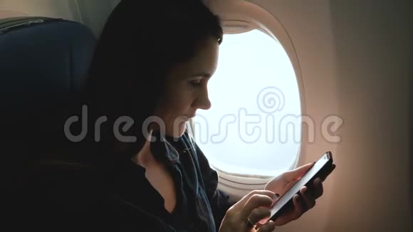 美丽的年轻快乐的高加索女商人使用智能手机电子商务应用程序在飞机窗口座位上飞行视频的预览图