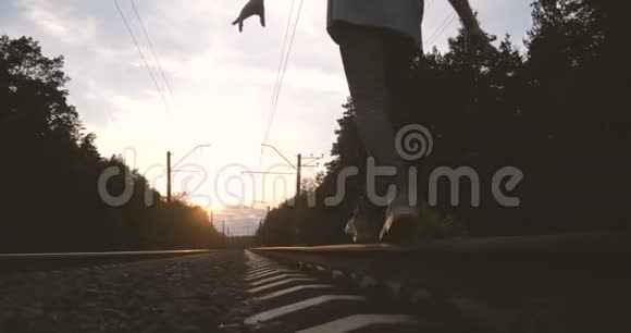 4K日落时一个年轻人沿着铁轨走着慢动作视频的预览图
