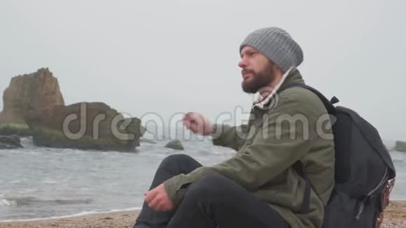 傍晚小胡子一个人坐在沙滩上把鹅卵石扔进水里视频的预览图