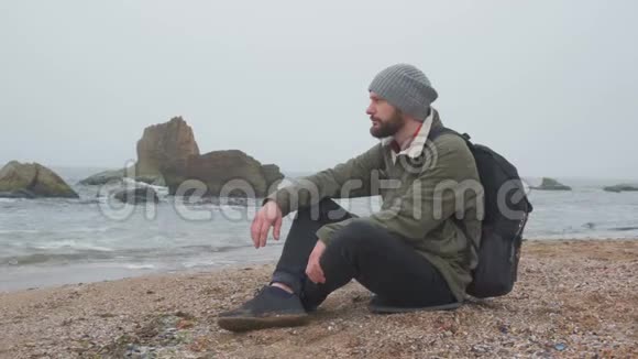 傍晚小胡子一个人坐在沙滩上把鹅卵石扔进水里视频的预览图